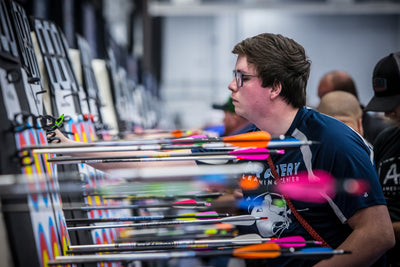An archer wearing an Archery Learning Center jersey marks his arrows after scoring.