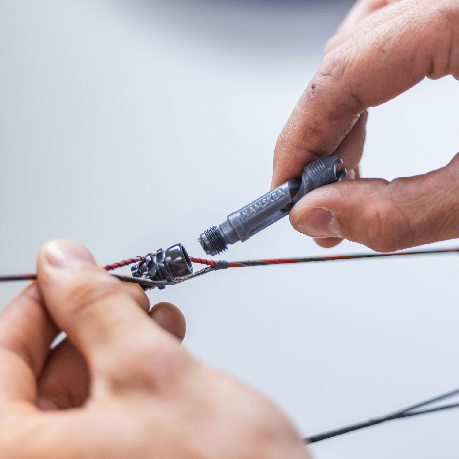Close-up of hands working with a compound bow string on a light background