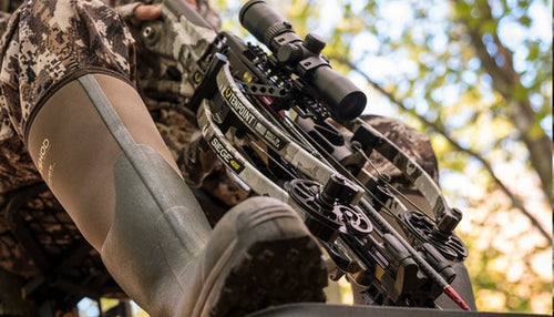 Close-up of a crossbow held by a person in camouflage clothing with a blurred natural background.
