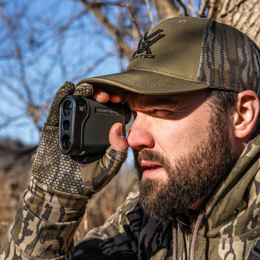 Man in hunting gear using a Vortex rangefinder outdoors.