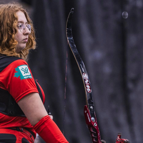 Person in red archery uniform with a bow, blurred background